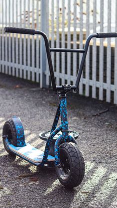 a blue scooter sitting on the ground next to a white fence and grass