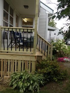 a wooden porch with chairs on it and flowers in the yard next to the house