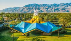 a large blue and yellow tent sitting in the middle of a lush green field next to mountains