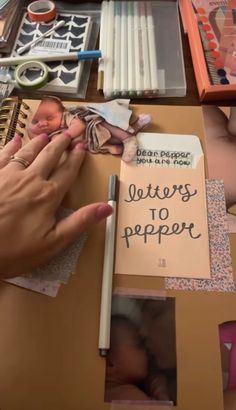 a person holding a pen over a baby's head and writing letters to paper