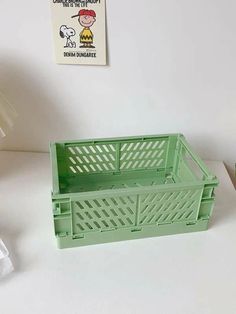 a green plastic crate sitting on top of a white table next to a lamp and pictures