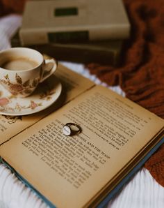 an open book with a ring sitting on top of it next to a cup and saucer