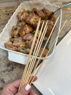 a person holding chopsticks over some food in a white dish on a counter