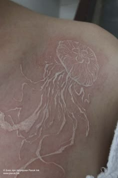 the back of a woman's shoulder with white ink on it and an image of a jellyfish