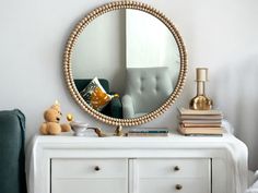 a mirror sitting on top of a white dresser next to a green chair and teddy bear