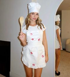 a girl in a chef's outfit is holding a spoon and posing for the camera