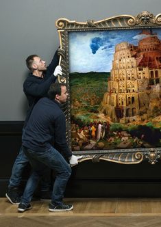 two men working on a large painting in an art gallery, one holding the frame