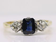 "This stunning ring holds an unusual emerald cut Sapphire, deep blue in colour flanked by two transitional cut sparkling Diamonds. The Sapphire weighs an approximate one carat and measures 4mm x 6mm and is in a six prong setting. Flanked by transitional cut Diamonds each weighing 0.25 carats a total of 0.50 carats. Quality:  H Colour  Clarity:  VS1 The ring dates Circa 1930's The Diamonds cut during this period, from about the 1920s through the 1940s, are often referred to in the trade as \"tran Gold Engagement Dress, Trilogy Ring, Engagement Dress, Antique Diamond Rings, Jewelry Workshop, Stunning Engagement Ring, Dress Rings, Gold Engagement, Sparkle Diamonds