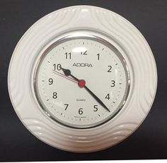 a white clock with red hands and numbers on it's face is shown against a black background