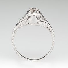 This pretty circa 1920s ring features a pierced design with engraved details and is centered with one (1) old European cut diamond that is prong set into a hexagonal shaped setting. The shoulders of the ring are each accented with one (1), bead set, round single cut diamond. The ring measures 7.1mm at the top, rises 7.3mm above the finger, tapering to 1.4mm wide and 0.7mm thick at the base of the shank. This ring is currently a size 7. The ring shows overall wear but has a nice fresh polish. Vintage Oval Diamond Ring With Single Diamond, Vintage Oval Diamond Ring With Single Stone, Classic Engraved Ring With Center Stone, Vintage Engraved Ring With Single Diamond For Formal Occasions, Antique Engraved Diamond Cut Promise Ring, Antique Engraved Promise Ring With Diamond Cut, Vintage Diamond Ring With Rose Cut Diamonds For Anniversary, Antique Diamond Cut Engraved Promise Ring, Antique Oval Single Diamond Ring