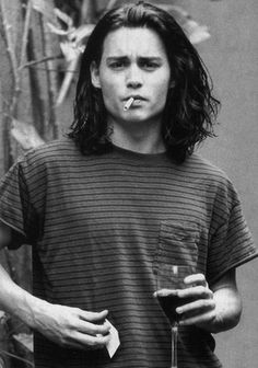 a black and white photo of a man with long hair holding a drink in his hand