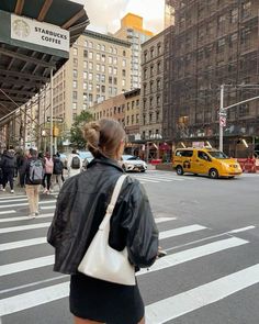 a woman is walking across the street in front of a yellow taxi and people crossing