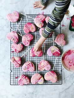 a person is decorating pink heart shaped cookies with icing on a wire rack