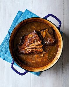 a pot filled with meat sitting on top of a blue cloth next to a wooden table