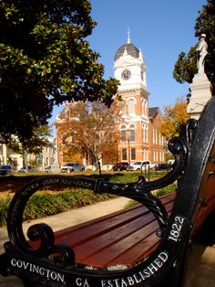 a wooden bench sitting in front of a building with a clock on it's side