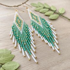 green and white beaded fringe earrings with gold accents on a wooden table next to leaves