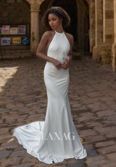 a woman in a white dress standing on a cobblestone walkway wearing a halter neck gown