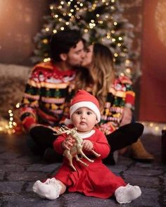 a baby sitting on the floor next to a christmas tree with his mother kissing him