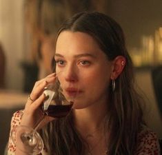 a woman sitting at a table with a glass of wine in front of her face