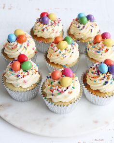 cupcakes with white frosting and sprinkles are arranged on a plate