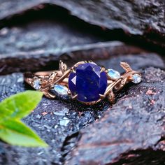 a gold ring with a blue stone in the middle on top of some rocks next to a leaf