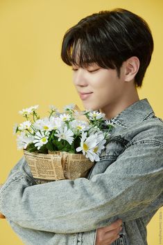 a young man is holding a basket with daisies in it and looking at the camera