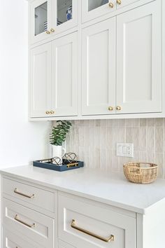 a kitchen with white cabinets and gold handles on the countertop, along with a plant in a basket