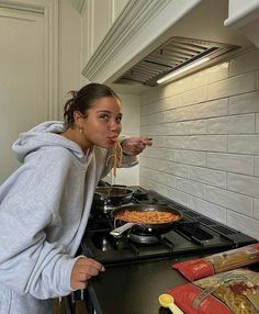 a woman standing in front of a stove with food on her face and holding a fork up to her mouth