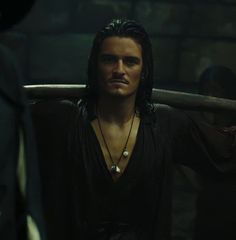 a man with long hair wearing a black shirt looking at another man in a dark room