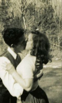 an old black and white photo of two people kissing each other in front of trees