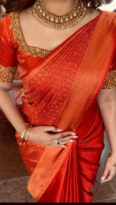 a woman in an orange sari with gold jewelry on her neck and hands behind her back