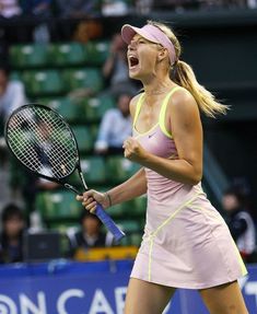 a woman holding a tennis racquet on top of a tennis court with people in the background