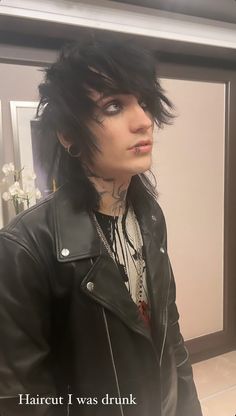 a man with black hair and piercings wearing a leather jacket in front of a mirror