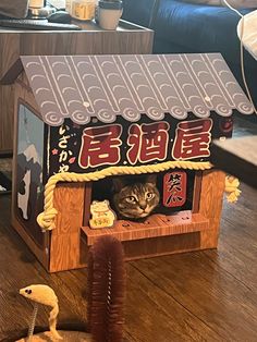 a cat is hiding in a dollhouse made out of wood and paper with chinese characters on the roof