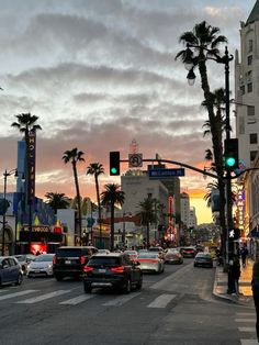 cars are stopped at an intersection in the city with palm trees and buildings on either side