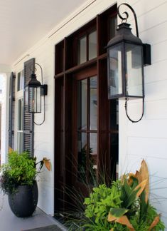 the front door of a white house with two large planters on it's porch