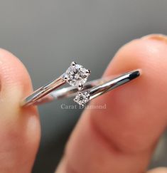 a close up of a person's hand holding a ring with two diamonds on it