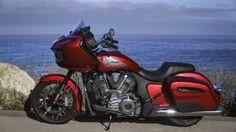 a red and black motorcycle parked next to the ocean