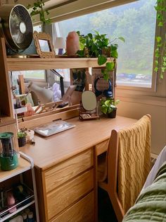 a desk with a fan, mirror and plants on it in front of a window