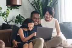 a man, woman and child sitting on a couch looking at a laptop