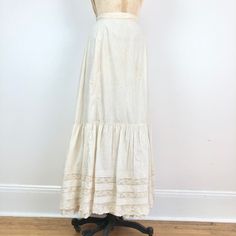 "Antique Victorian white cotton maxi skirt has a 3 layered hem with the a lace inset and pin tuck top layer. The skirt has a gathered back waist. Condition Structurally good condition, missing the back waist closure entirely, and has overall yellowing. There are small stains across the center front hip area and right hip. There are more stains at the back left hip area and center area. Has small splits between the lace inset and cotton throughout the hem, and some small holes in the lace. There' Cream Cotton Ruffled Skirt, Beige Cotton Skirt With Lace Trim, White Fitted Tiered Maxi Skirt, Daywear Long Lace Skirt, White Ruffled Maxi Skirt For Daywear, Elegant Ruffled Maxi Skirt For Daywear, Vintage Tiered Skirt In Cream, Vintage Cream Tiered Skirt, Tiered Cotton Skirt With Lace Trim