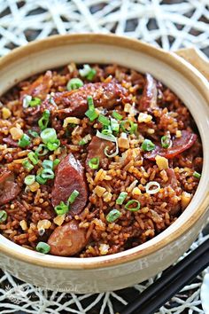 a wooden bowl filled with rice and meat on top of a table next to chopsticks