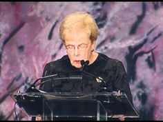 an older woman standing at a podium making a speech