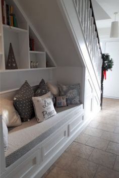 a room that has some pillows on the bench in front of it and stairs leading up to the second floor