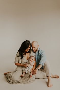 a man and woman sit on the floor with their baby in front of them, both holding