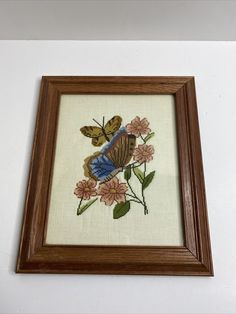 an embroidered picture frame with a butterfly and flowers in the center on a white wall