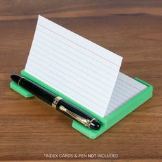 a pen and note pad sitting on top of a wooden table next to a green holder