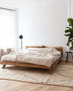 a bed sitting on top of a wooden floor next to a plant in a bedroom