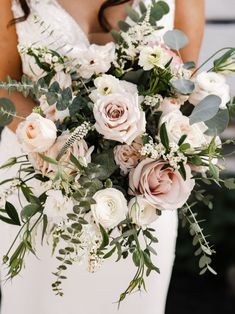 a bride holding a bouquet of white and pink flowers with greenery in her hands