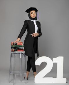 a woman in a graduation gown is standing next to a table with stacks of books